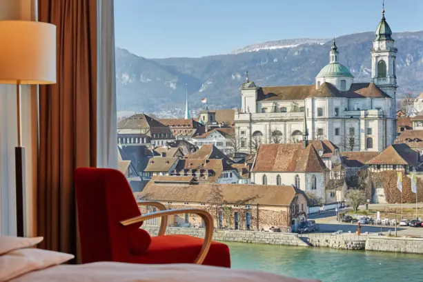 Detailierte Aufnahme im Hotelzimmer auf einen roten Stuhl vor einem Fenster. Durch das Fenster blcikt man auf den Fluss Aare.