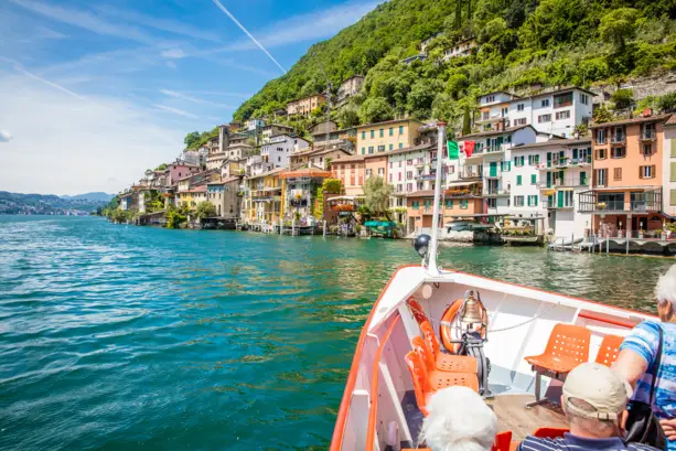 Aufnahme auf einem kleinen Boot, welches über den Lago Maggiore fährt. Direkt am Wasser stehen mehrere Häuser.