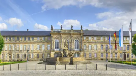 Eingangsbereich mit einem großem Platz vom neuen Schloss. Davor ist ein großer Brunnen mit Figuren.