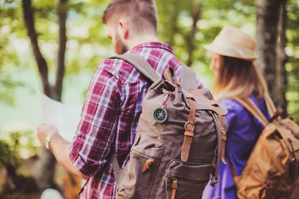 Pärchen von hinten mit großen Wanderrucksäcken in einem Wald.